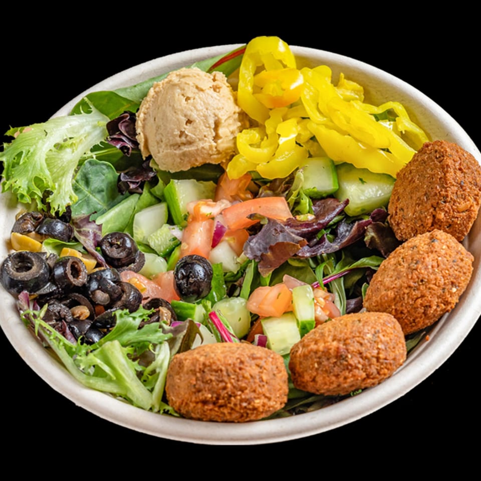 A healthy Bowls N Go falafel bowl with hummus, olives, peppers, and fresh greens.