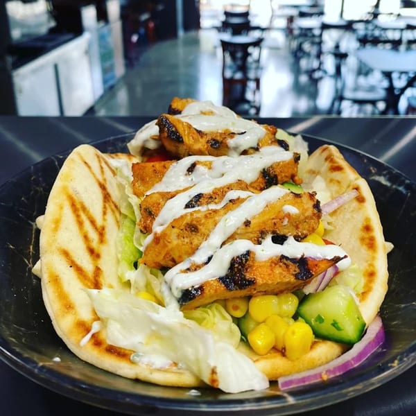 Grilled chicken, lettuce, corn, cucumber, and red onion on pita bread, drizzled with white sauce.