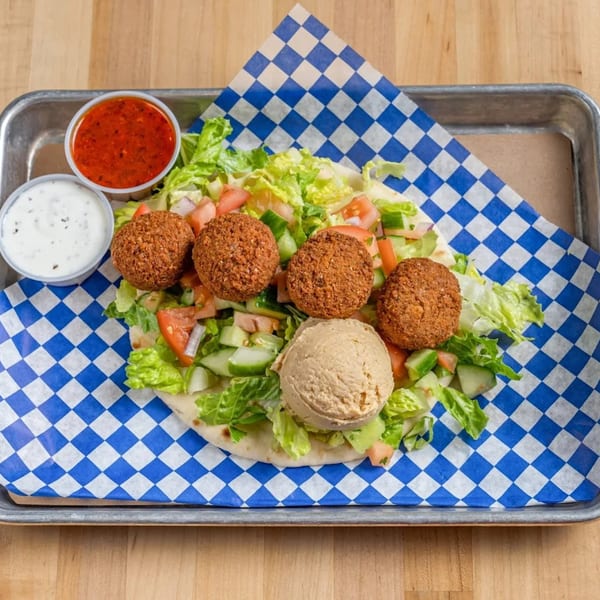Falafel, hummus, and salad on pita bread with red and white sauces on a metal tray.