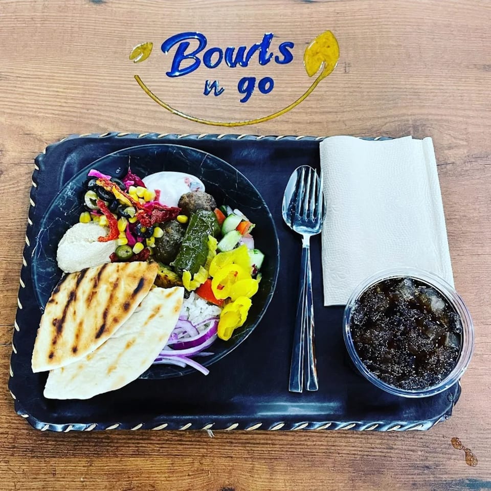 A healthy Bowls N Go meal with grilled pita, hummus, salad, and a drink on a tray.