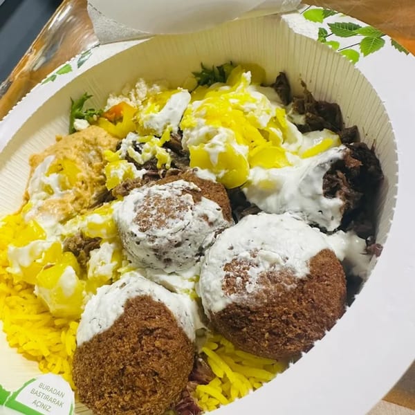 A healthy bowl from Bowls N Go with falafel, yellow rice, meat, and various sauces.