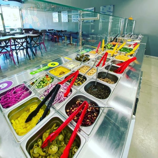 A vibrant self-serve salad bar at Bowls N Go, filled with fresh ingredients and colorful tongs.