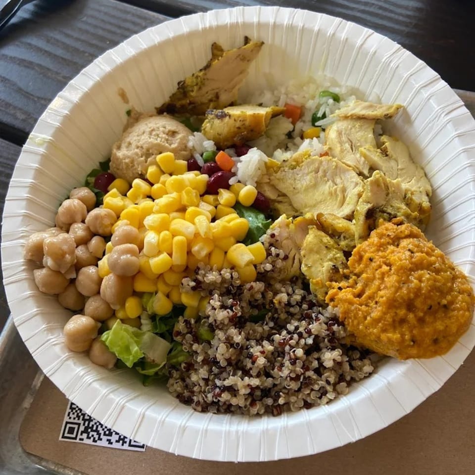 A healthy Bowls N Go bowl with chicken, rice, quinoa, chickpeas, corn, and red sauce.