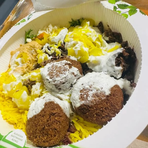 A Bowls N Go falafel bowl with yellow rice, meat, and white sauce in a takeout container.