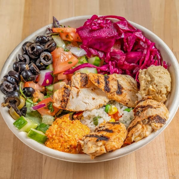 A healthy Bowls N Go bowl with grilled chicken, rice, olives, red cabbage, hummus, and vegetables.