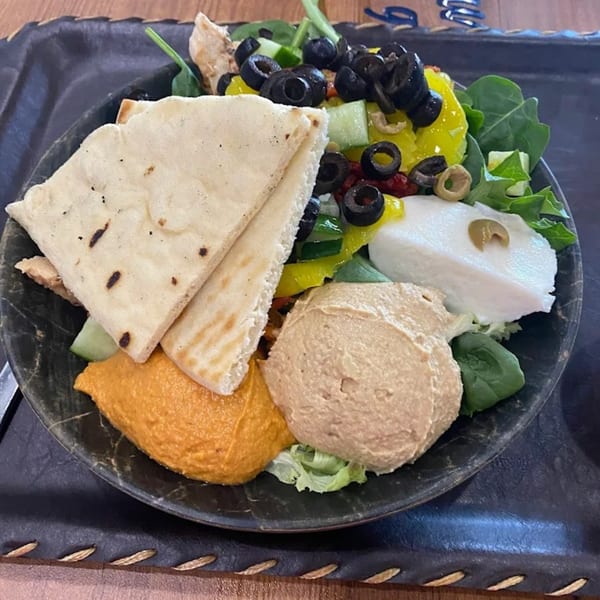 A healthy bowl with pita bread, hummus, red pepper hummus, mozzarella, olives, and greens.