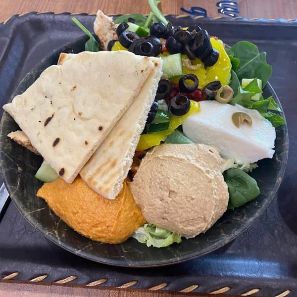 A healthy bowl with pita bread, hummus, red pepper hummus, mozzarella, olives, and greens.