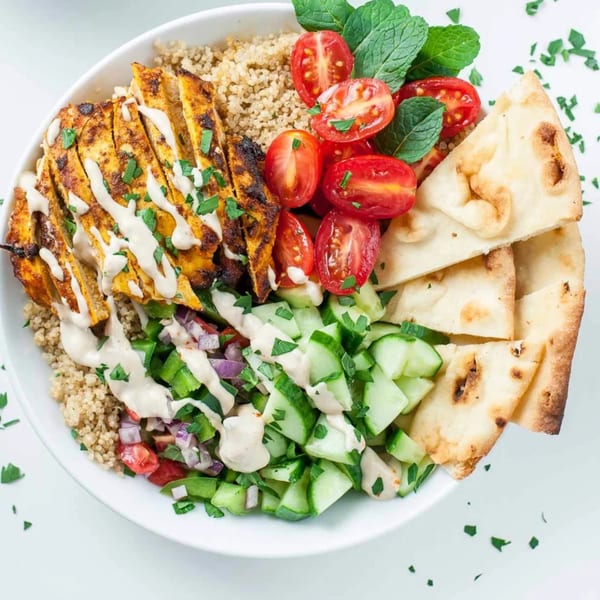 A healthy Bowls N Go bowl with grilled chicken, quinoa, tomatoes, cucumbers, and pita bread.